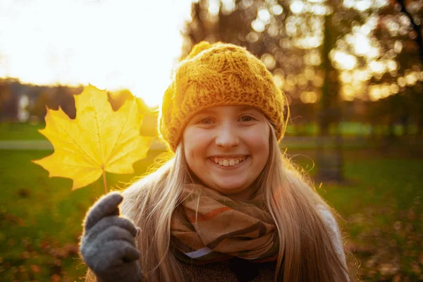 城市公园里穿着棕色毛衣 头戴橙色帽子 在户外展示秋天叶子的快乐小孩的画像 — 图库照片
