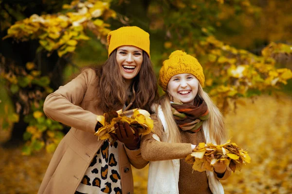 안녕하 가을에는 공원의 야외에서 노란색 모자를 모녀가 웃으며 나뭇잎을 던진다 — 스톡 사진