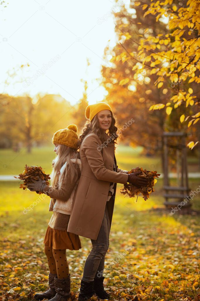 Hello autumn. smiling young mother and child in orange hats outdoors on the city park in autumn throws up autumn leaves.