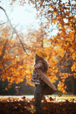 Merhaba Ekim. Gülümseyen modaya uyan 40 yaşındaki bej ceketli ve turuncu şapkalı kadın sonbaharda şehir parkında neşe içinde..