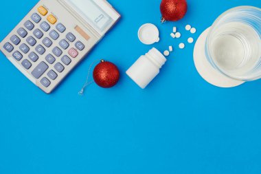 flat lay with christmas ball, pills, glass of water and calculator on blue background.