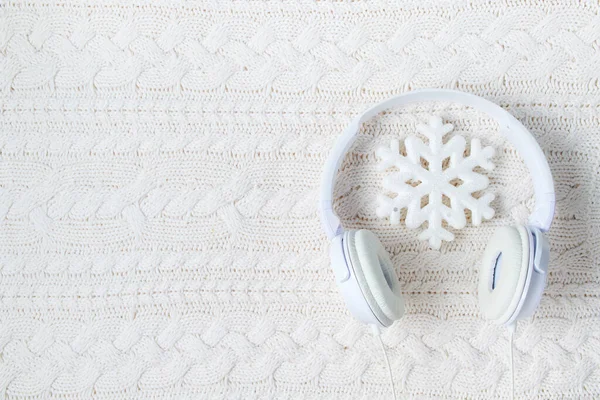 winter flat lay with white headphones and snowflake on white knitted background.