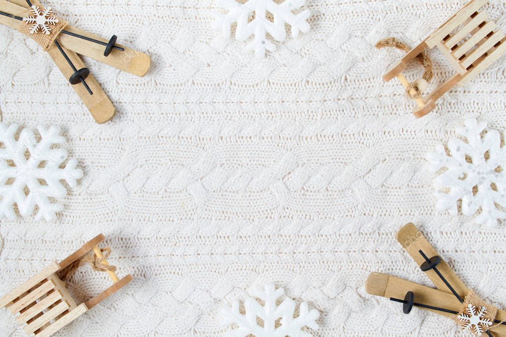 winter flat lay with snowflakes, sleds and skis on white knitted background.
