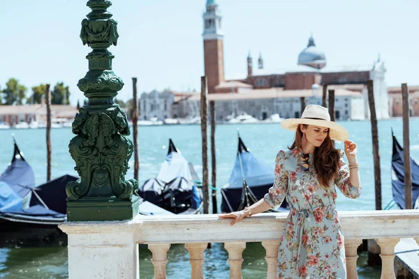 イタリアのヴェネツィアの堤防上のサングラスや帽子を持つ花のドレスの現代の観光客の女性 — ストック写真