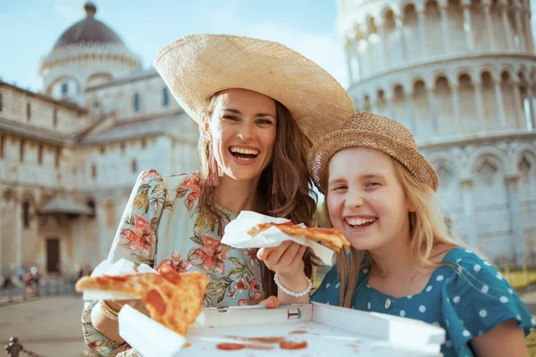 Portrait of smiling stylish family with pizza near Leaning Tower in Pisa, Italy.