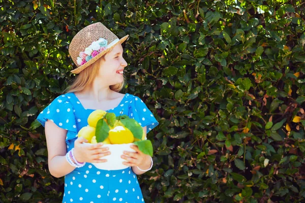 全体的に青で幸せな流行の子供と緑の壁の近くに屋外地元の農場レモンのプレートと帽子 — ストック写真