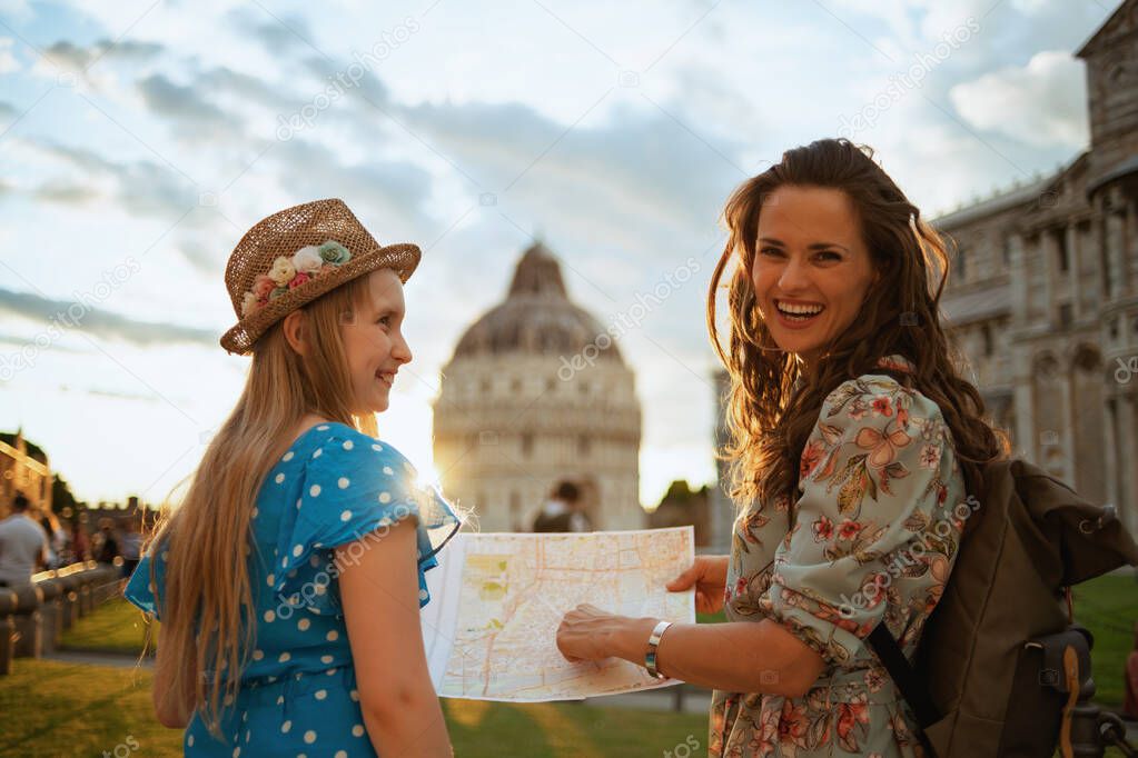 happy stylish mother and daughter with map and backpack enjoying promenade in square of miracles in Pisa, Italy.