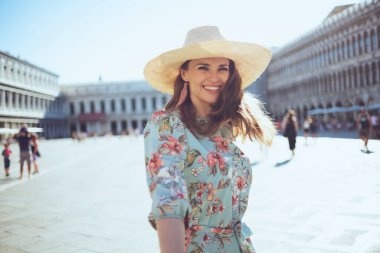 Çiçekli elbiseli, gülümseyen genç turist kadın Venedik, İtalya 'daki Piazza San Marco' da gezinti yapıyor..