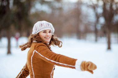Eldivenli, örgü şapkalı, koyun derisi ceketli zarif orta yaşlı kadın kışın şehir parkında neşe içinde eğleniyor..