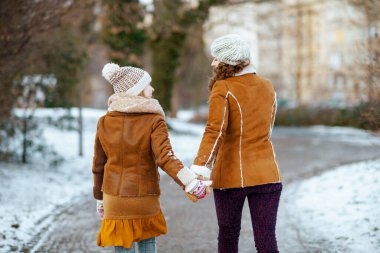 Örgü şapkalı ve kuzu derisi ceketli, örgü şapkalı ve koyun derisi ceketli anne ve çocuğun kışın şehir parkında yürüdüğünü gördüm..
