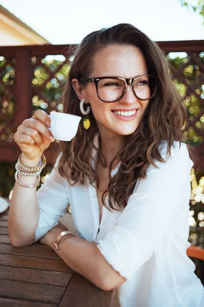 Usměvavá Stylová Hospodyňka Bílé Košili Šálkem Kávy Brýlemi Sedící Stolu — Stock fotografie