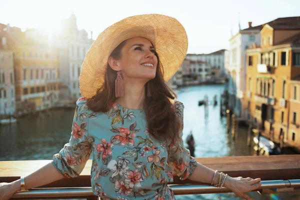 現代的な中年の旅行者の女性を笑顔花のドレスで帽子を楽しみます遊歩道でヴェネツィアのアカデミア橋 イタリア — ストック写真