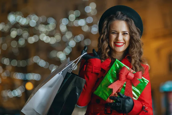 冬の楽しみ 赤いコートと黒のベレー帽を着た幸せな現代女性の買い物客の肖像ショッピングバッグと夜の街の外の贈り物 — ストック写真