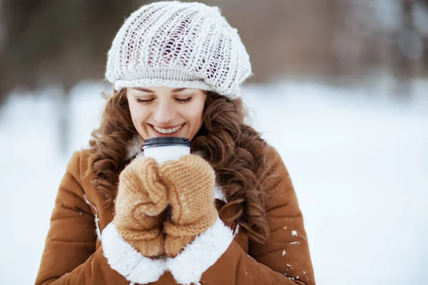 ニット帽と羊の皮のコートを着たミトンとホットドリンクのカップを持つ幸せなスタイリッシュな女性冬に市内公園の外 — ストック写真