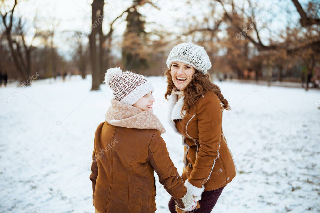 smiling elegant mother and child in a knitted hats and sheepskin coats with mittens in a knitted hat and sheepskin coat outdoors in the city park in winter.