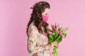elegantní žena středního věku s dlouhými vlnité brunetky vlasy s tulipány kytice a růžová maska proti růžové pozadí.