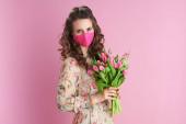 mladá 40 let stará žena s dlouhými vlnitými brunetkami vlasy s tulipány kytice a růžová maska izolované na růžové.