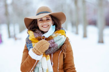 Kahverengi şapkalı, atkılı, eldivenli, kuzu derisi ceketli modern bir kadın kışın şehir parkında..