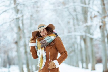 Kahverengi şapkalı ve atkılı modern orta yaşlı kadın. Kışın şehir parkında koyun derisi ceketli eldiven takıyor..