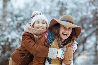 gülümseyen modern anne ve çocuk şapkalar ve koyun derisi ceketler ile şehir parkında kışın kucaklaşan eldivenler..