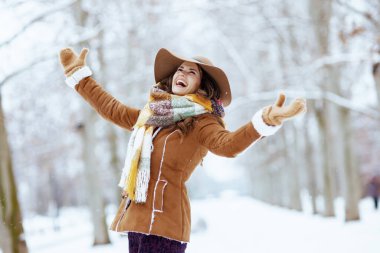 Kahverengi şapkalı ve atkılı mutlu bir kadın. Koyun derisi ceketli eldivenli. Kışın şehir parkında neşeli bir şekilde..