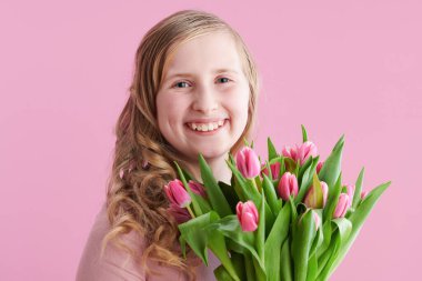 Gülümseyen stil çocuğunun portresi pembe arka planda izole edilmiş uzun dalgalı sarı saçlı ve lale buketli.