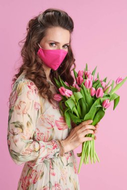 Uzun dalgalı esmer saçlı, lale buketli ve pembe maskeli, modaya uygun orta yaşlı kadın..