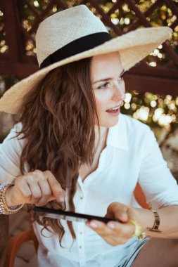 Pansiyon otelinin terasında akıllı telefon uygulamaları kullanan beyaz gömlekli, modaya uygun bir kadın..