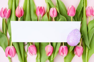 Paskalya yumurtası, kağıt çarşaf ve pembe arka planda izole lalelerle bezenmiş..