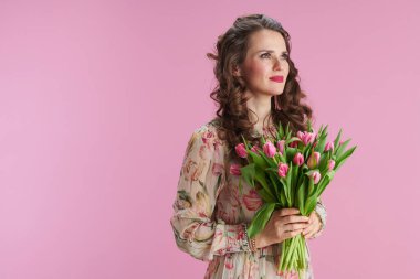Gülümseyen orta yaşlı, çiçekli bir kadın pembe arka planda izole edilmiş laleler..