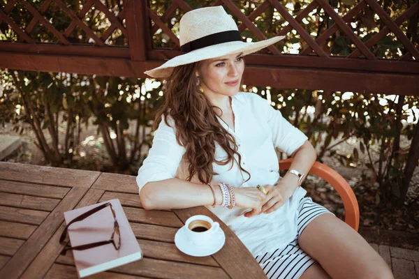 ゲストハウスホテルのテラスにあるテーブルに座っているコーヒー 眼鏡をかけた白いシャツの現代的な主婦 — ストック写真