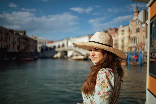 意大利威尼斯Rialto桥附近 一名身穿花衣 戴着帽子和医疗面具的年轻女子在路堤上 — 图库照片