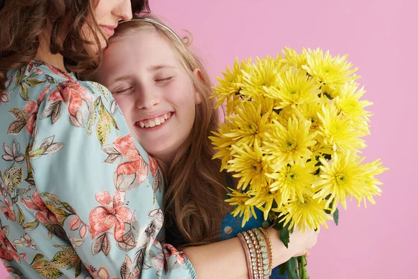 笑着的现代母女 长长的波浪般的头发 黄色的菊花花朵 抱着粉红的背景 — 图库照片