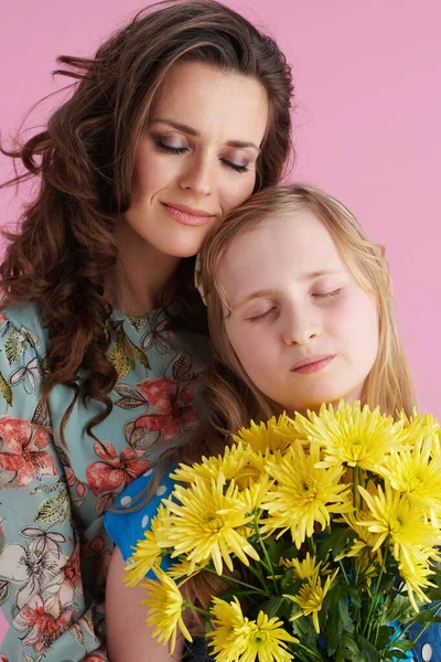 轻松自在的现代母亲和孩子 留着长长的波浪般的头发 黄色的菊花 背景是粉红色的 — 图库照片