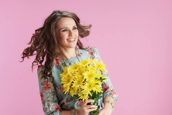 happy stylish 40 years old woman with long wavy brunette hair with yellow chrysanthemums flowers isolated on pink.