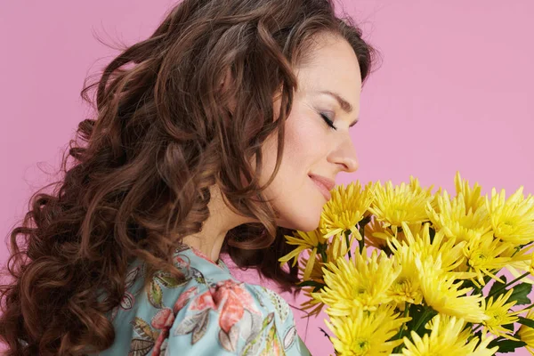 ピンクを背景に黄色の菊の花を持つ花のドレスでリラックスしたスタイリッシュな女性 — ストック写真