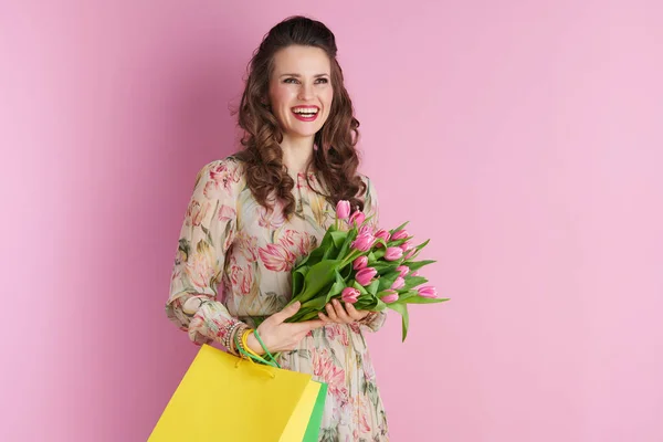 幸せなスタイリッシュな女性とともに長い波状ブルネットの髪でチューリップ花束とショッピングバッグ隔離されたピンク — ストック写真