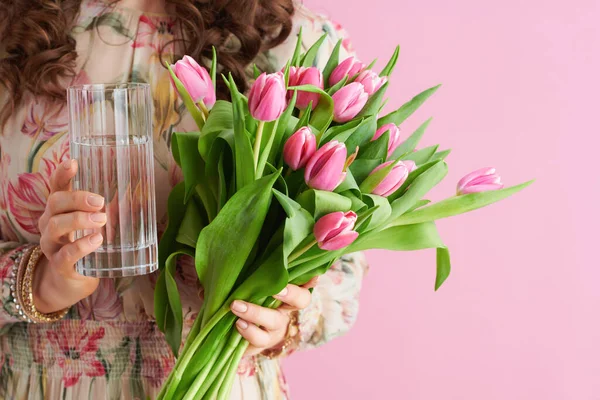 閉鎖上の中年女性とともにチューリップ花束とガラスの水に対してピンクの背景 — ストック写真