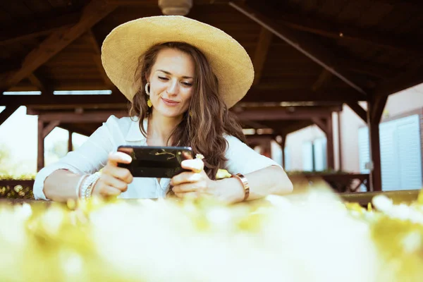 Beyaz Tişörtlü Sırıtan Şapkalı Bir Kadın Çiftlikte Akıllı Telefon Kullanarak — Stok fotoğraf