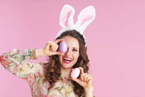 穿着花裙子的年轻女人 长着小兔子耳朵 有一个粉色背景的复活节蛋 — 图库照片