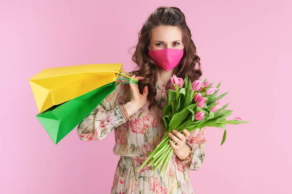 ピンクで隔離されたチューリップの花束 ピンクのマスクとショッピングバッグと花のドレスのスタイリッシュな女性 — ストック写真