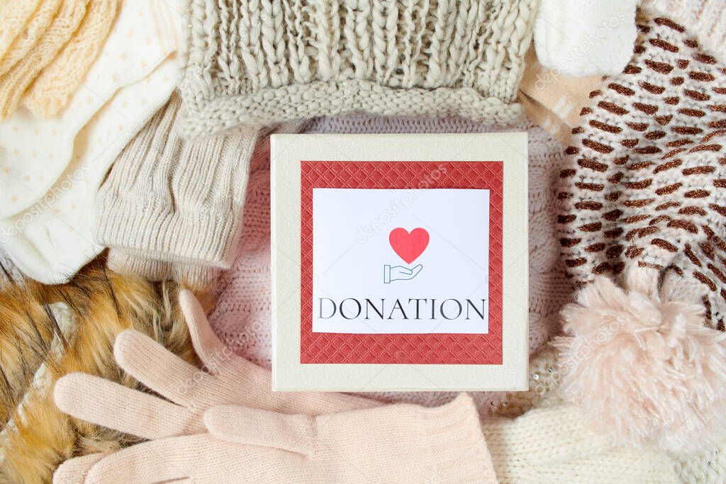 winter flat lay with mittens, hats, winter clothes and donation box on white knitted background.