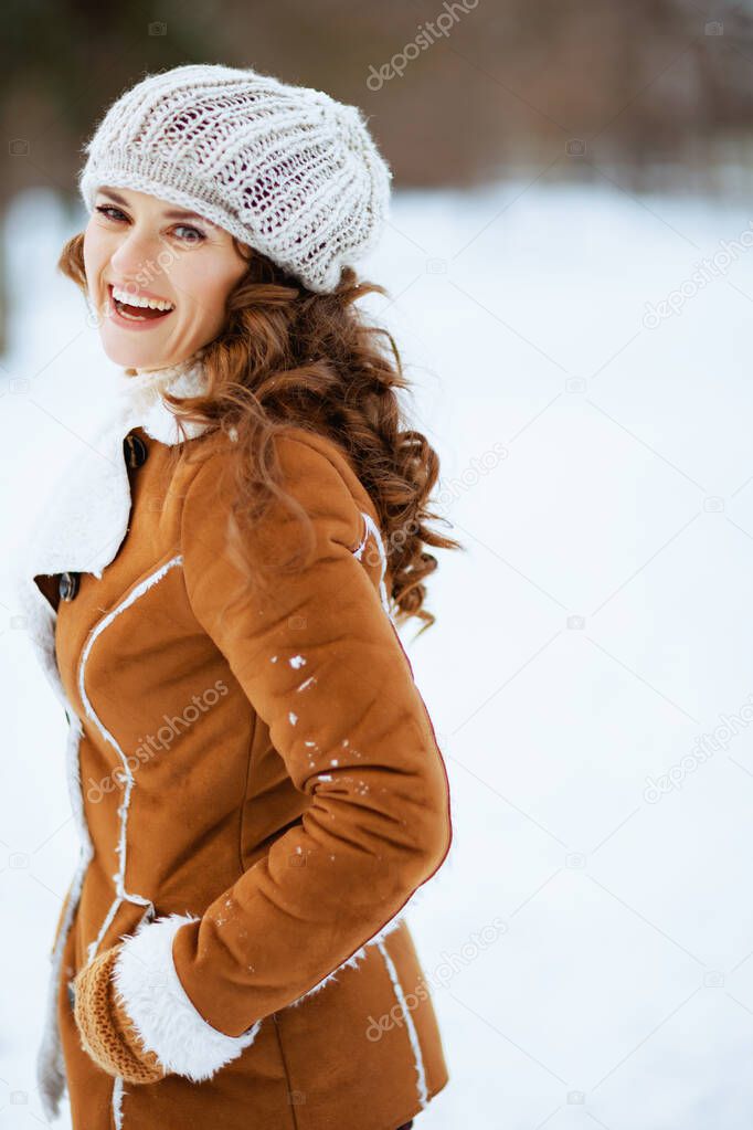 smiling modern middle aged woman outdoors in the city park in winter in a knitted hat and sheepskin coat walking.