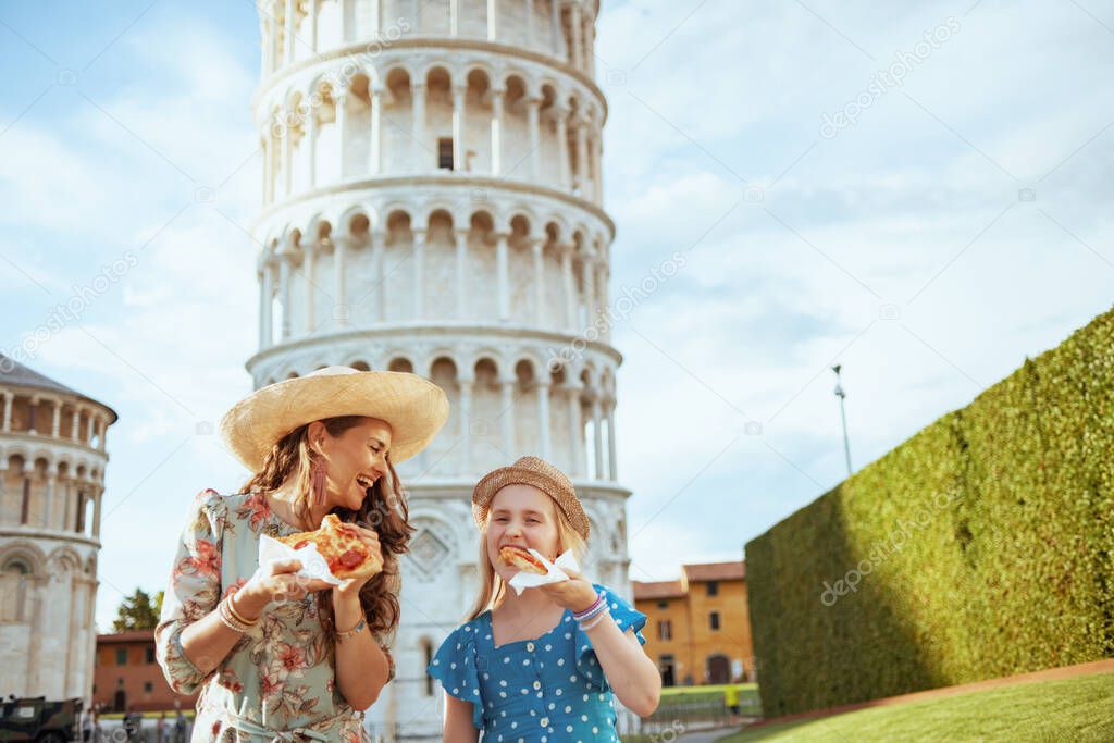 smiling stylish mother and daughter with pizza near Leaning Tower in Pisa, Italy.