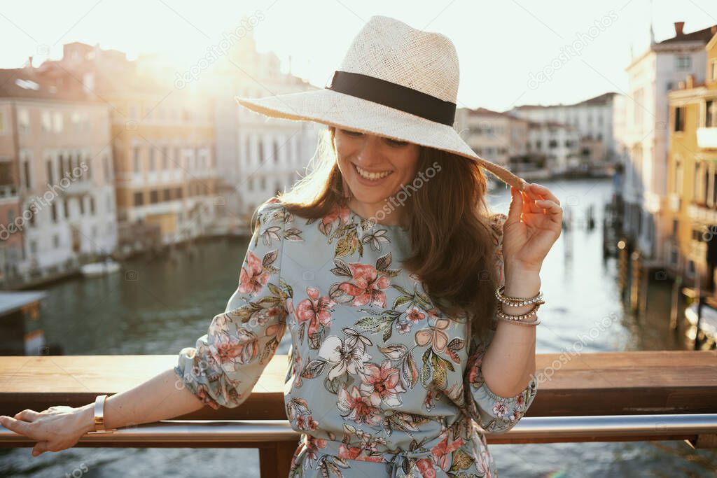 happy stylish solo tourist woman in floral dress with hat on Accademia bridge in Venice, Italy.