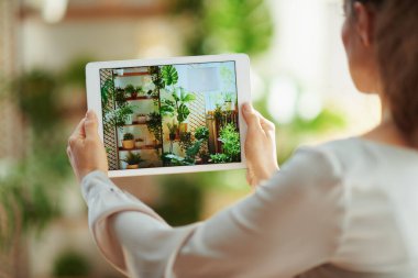İç mekan videosu. Güneşli bir günde modern evde tabletli genç kadın fotoğrafçı tarafından görüldü..
