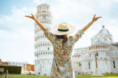 İtalya, Pisa 'da Leaning Tower' ın yanında çiçek desenli şapkalı turist bir kadının arkasından sevinçle kollarını açarken görüldü..