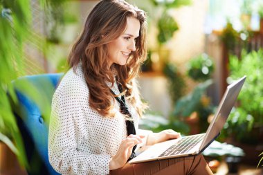 Yeşil Ev. Güneşli bir günde modern evde dizüstü bilgisayarı olan uzun dalgalı saçlı mutlu modern bir kadın..