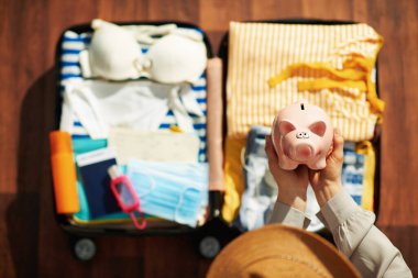 Covid-19 salgını sırasında seyahat et. Modern kadının dezenfektan, tramvay çantası, tıbbi maske, domuz kumbarası ve güneşli bir günde modern evdeki spa manzarası..