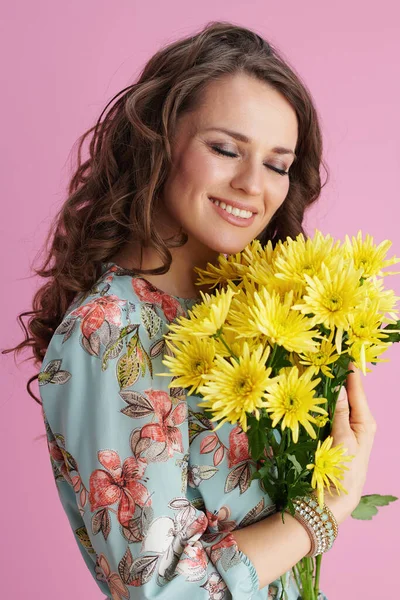 笑容可亲的中年妇女 一头长长的波浪般的黑发 黄菊花丛生 背景是粉红色的 — 图库照片